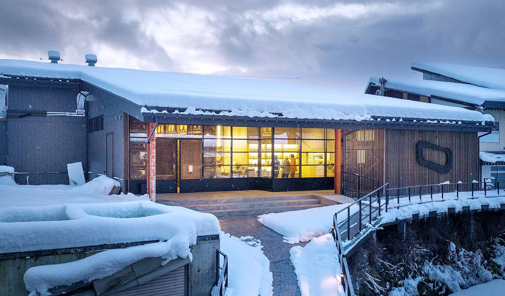 雪に覆われた冬の風景の中に建つ、大きなガラス窓が特徴のモダンな建物です。